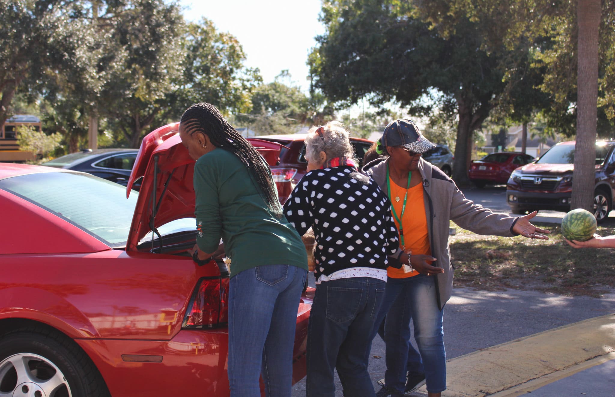 Volunteers load food into trunk of red car.