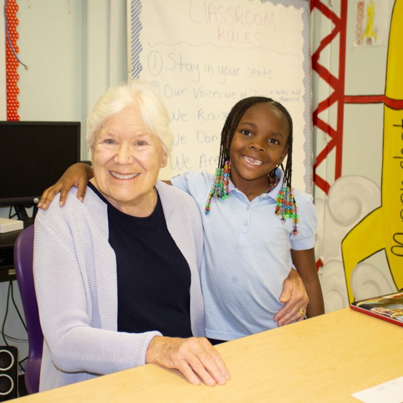 Photo of GYAC volunteer, Ginny Hiland, and first-grade student, smiling.